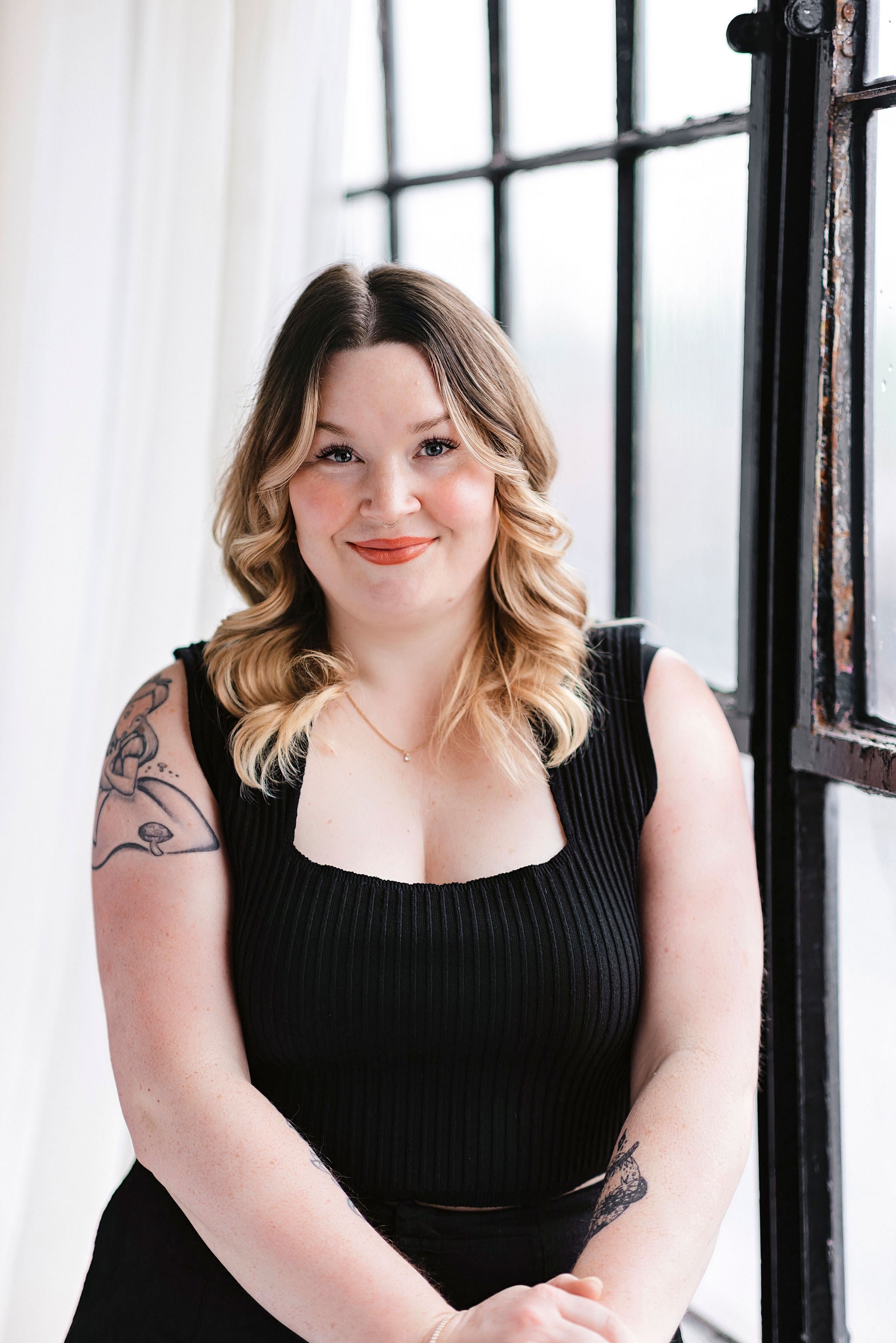 Woman with tattoos wearing a black sleeveless top in a softly lit room.