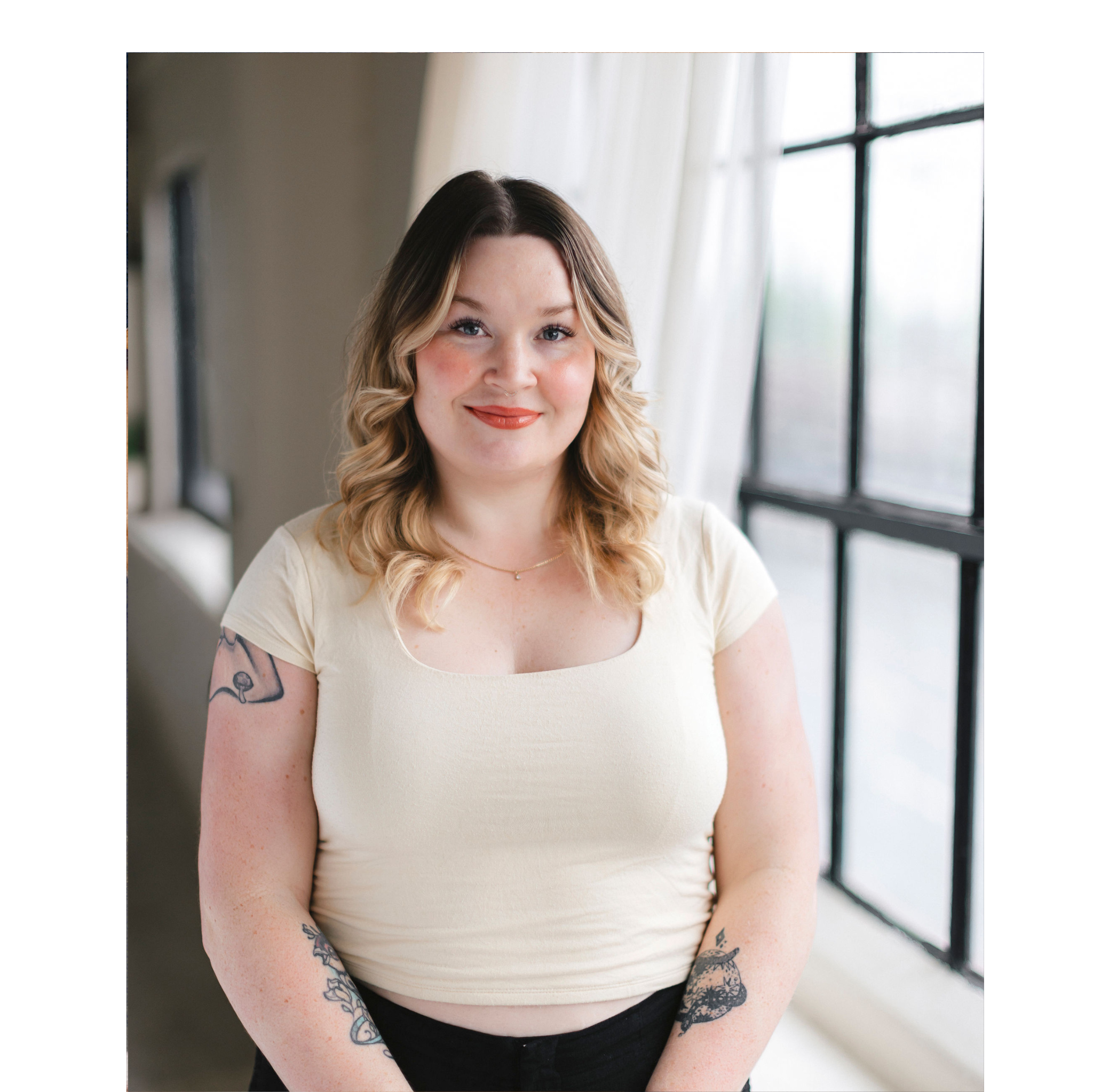 Woman with tattoos wearing a white top in a softly lit room.