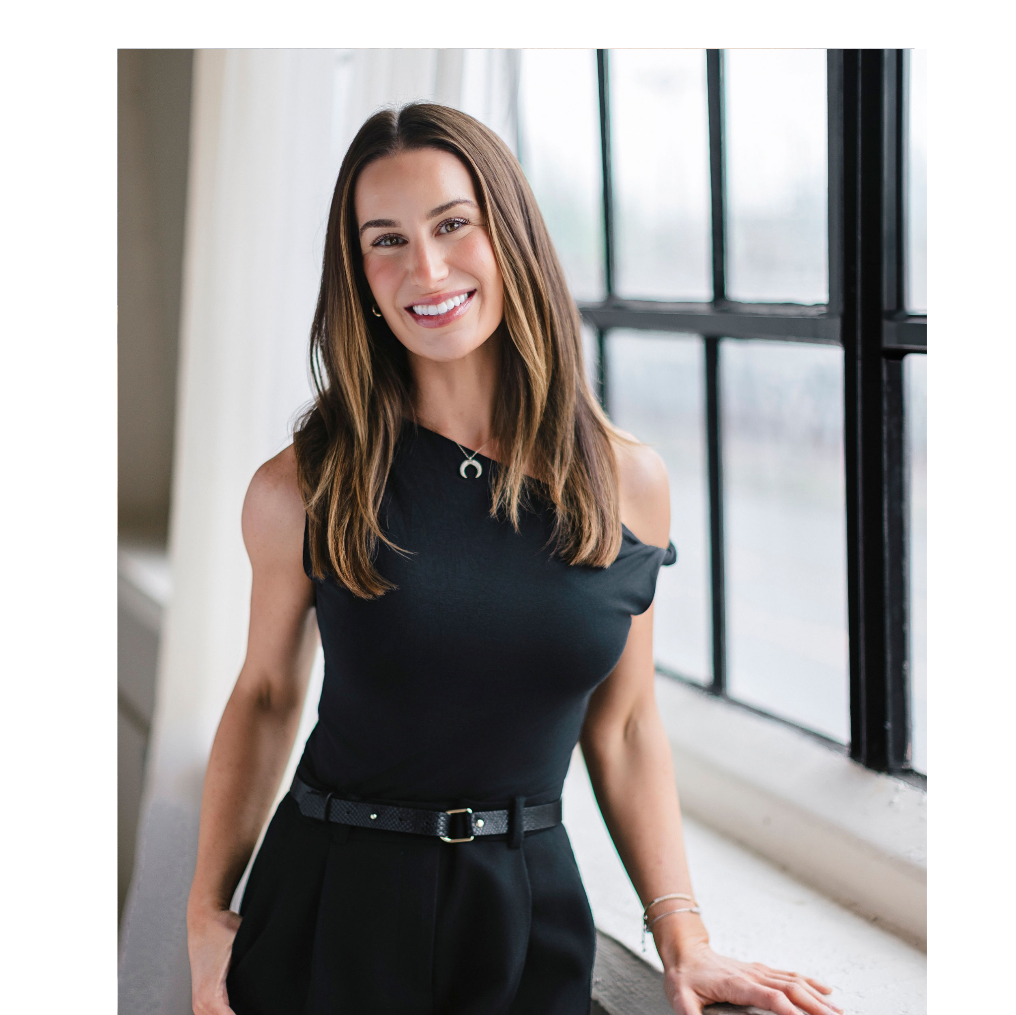 Woman in a black dress standing in a room with large windows.
