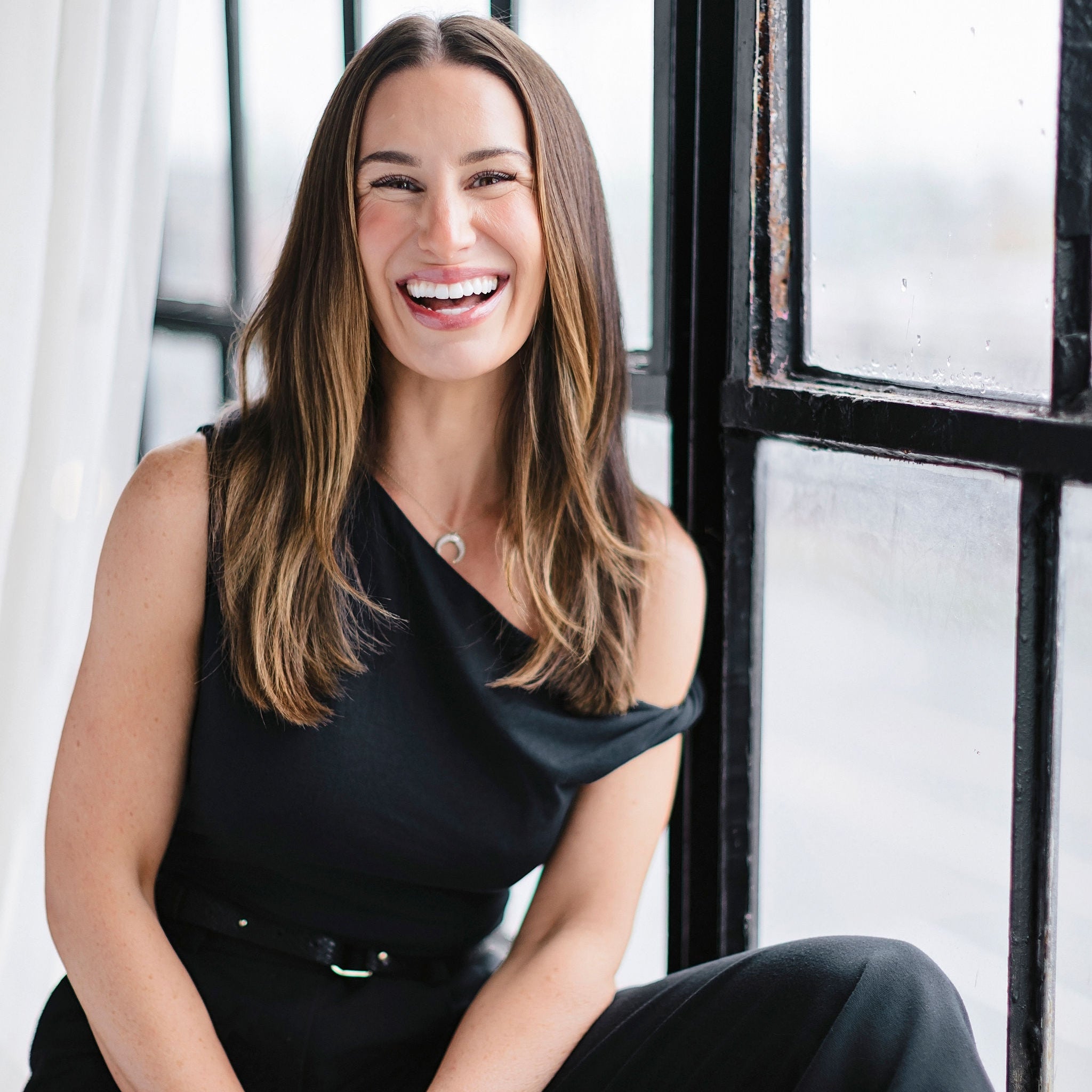 Woman in a black outfit sitting in front of a large window