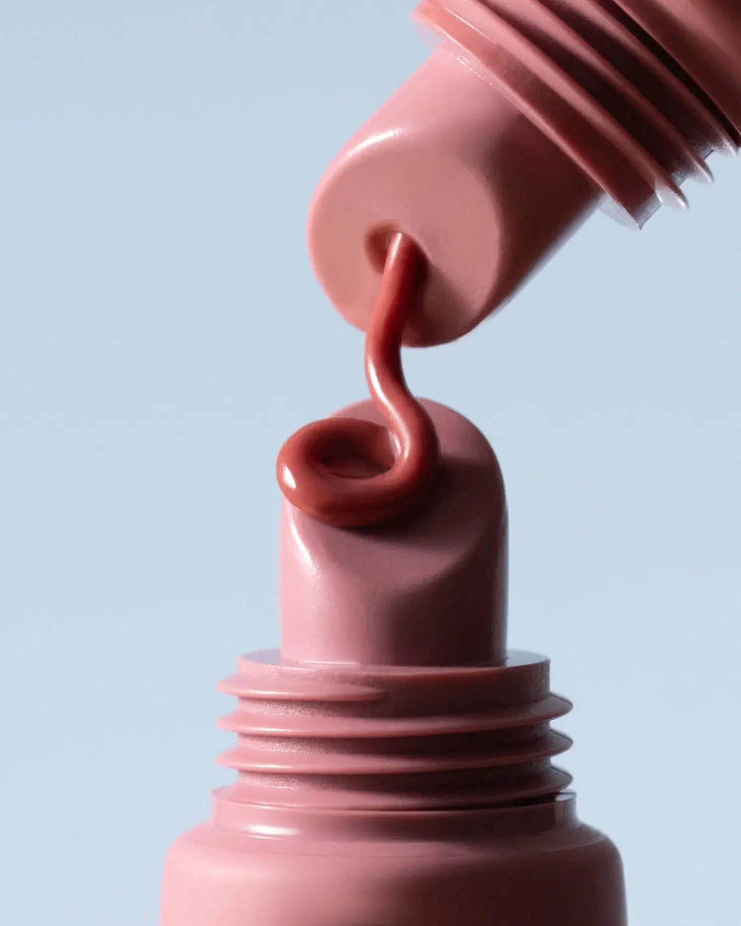 Close-up of a pink lipstick being applied with a brush on a light blue background