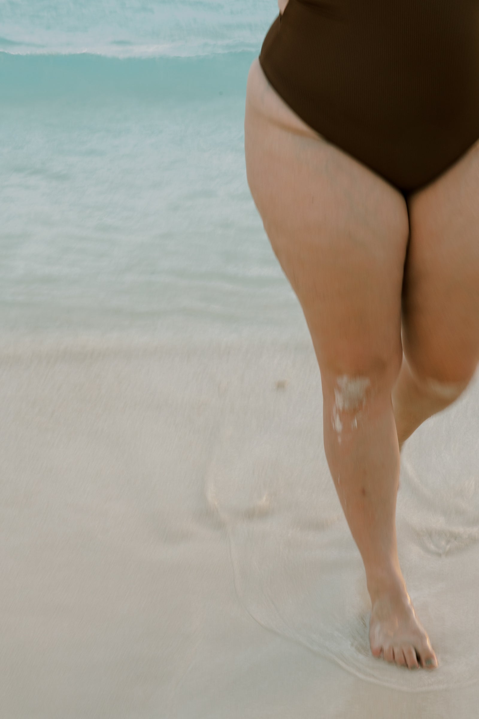 Person wearing a brown swimsuit standing on a sandy beach