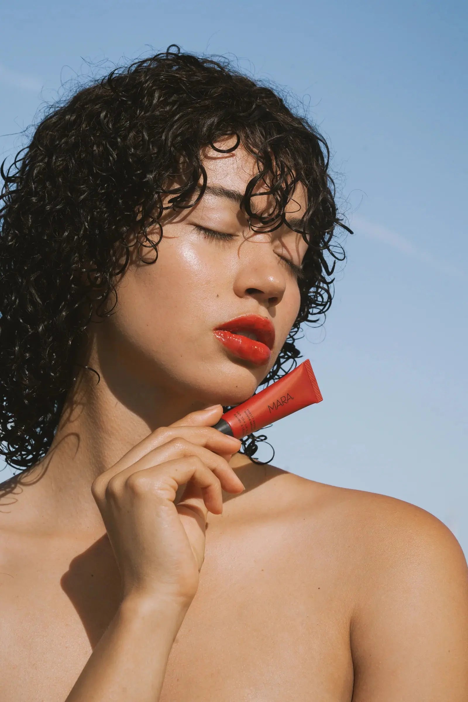 Women outdoors wearing Toasty Rouge lip balm holding red tube