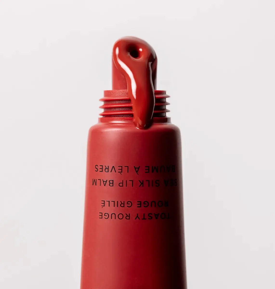 Red lip balm with a white cap on a light gray background